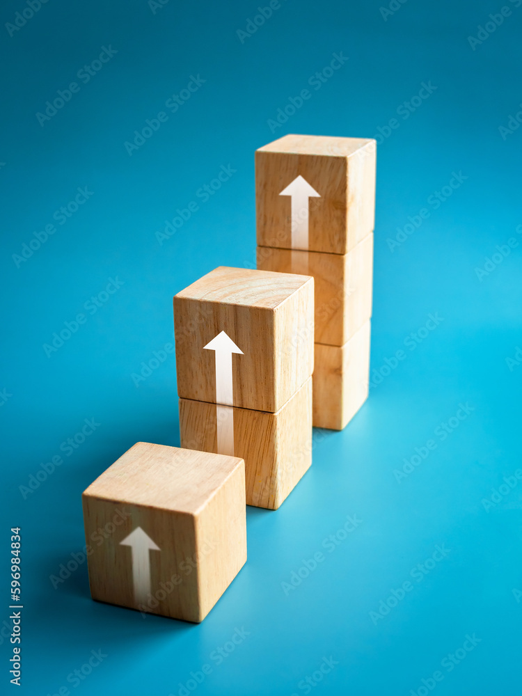 Aufkleber rising up arrows shining on wooden cube blocks bar graph chart steps on blue vertical background, mi