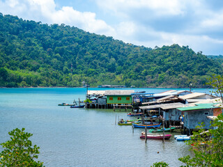 Fototapeta na wymiar Ao Yai village, Koh kood, trat, Thailand. Scene of fisherman local village with many house in the tropical blue sea and green mountain with beautiful view with open sky on summer sunshine day.