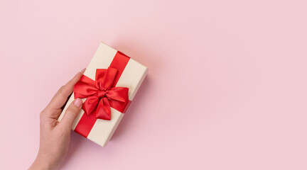 Hands holding gift box with red bow on pink background. Top view