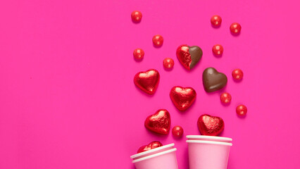 Wrapped and unwrapped heart shape chocolate candies in red foil on pink background