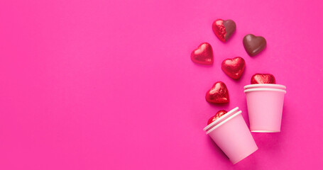 Wrapped and unwrapped heart shape chocolate candies in red foil on pink background