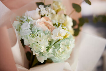 festive bouquet of flowers on the table. Glass vase with a bouquet of beautiful flowers on the table in the room. Place for text. Beautiful bouquet in a festive package on the table
