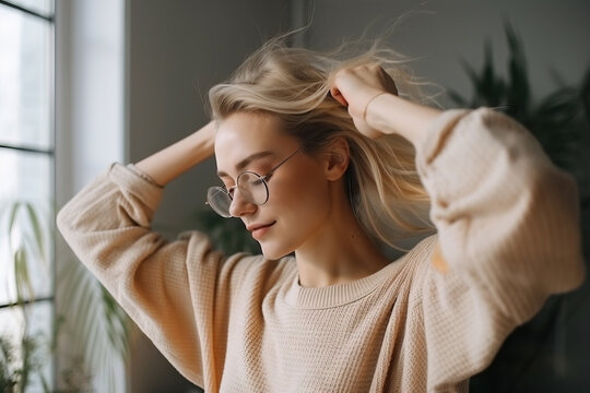 Funny young fair-skinned woman dancing with her eyes closed alone at home in daytime. Blonde with hair pulled back wears translucent glasses and oversized sweater. Generative AI