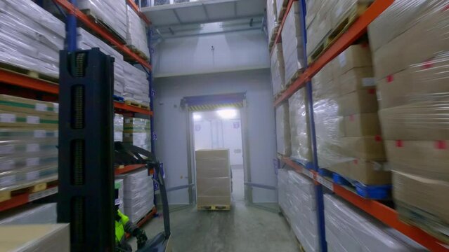 FPV drone view of forklifts moving frozen food cargo in huge warehouse