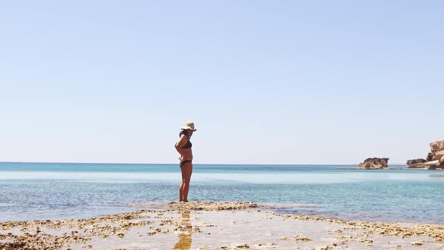Young girl looking at camera stand on rocky formations by sea cave near Paphos, Cypris. A shot from the inside of a sea cave in sunny Mediterranean coast of Cyprus.Grotto sea cave