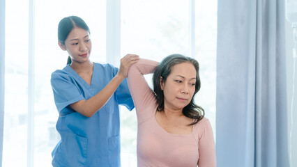 Asian Chinese female physiotherapist caregiver helping elderly woman exercise for recovery, prevention of osteoarthritis and osteoporosis.