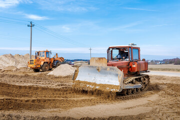 An old orange bulldozer performs work to level the sandy soil