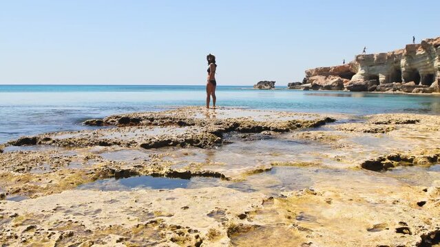 Young girl looking stand on rocky formations by sea cave in Ayia Napa, Cyprus. A shot from the inside of a sea cave in sunny Mediterranean coast of greek Cyprus.Grotto sea cave