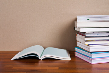 A stack of books on a wooden floor with one open book and one open book on the right.