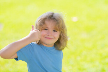 Close up portrait of funny kids face with thumb up. Portrait of kid outdoors. Close-up face child playing outdoors in summer park.