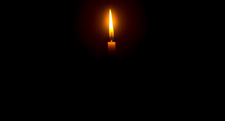 A single burning candle flame or light glowing on an orange candle on black or dark background on table in church for Christmas, funeral or memorial service with copy space