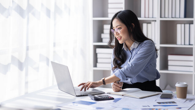 Asian Business woman using calculator and laptop for doing math finance on an office desk, tax, report, accounting, statistics, and analytical research concept
