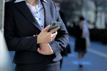 屋外で立ち止まってスマホを操作しているビジネスウーマン