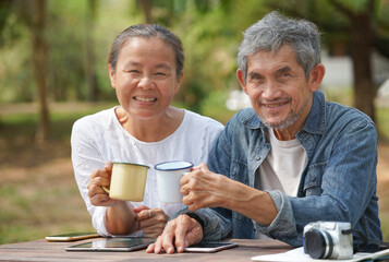 happy senior couple sitting together and looking at camera,old tourist people relaxing at resort garden in the countryside,concept of elderly pensioner travelling,health benefit in nature,wellbeing