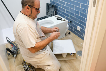 Senior plumber installer installing toilet in a bathroom.