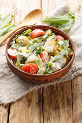 Fresh salad of eggs, potatoes, tomatoes and sorrel seasoned with cream sauce close-up in a bowl on a wooden table. Vertical