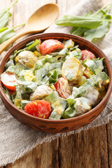 Salad of boiled eggs, potatoes, tomatoes and fresh herbs seasoned with cream sauce close-up in a bowl on a wooden table. Vertical