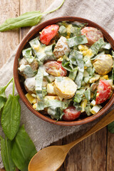 Breakfast healthy salad of boiled eggs, potatoes, tomatoes, onions and sorrel, spinach with cream dressing close-up in a bowl on a wooden table. Vertical top view from above