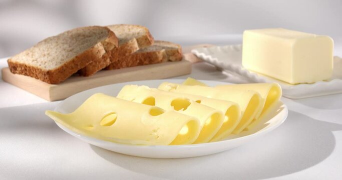dairy products on a light background. cheese bread and butter on a white tablecloth close-up. slices of gouda cheese. piece of butter and slices of bread in the background.