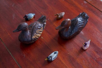 Two wooden ducks and four plastic ducks over a wood table.