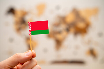 Belarus flag in mans hand on the wooden world map background. Global economy and geopolitics...