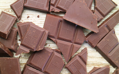 Heap of cracked dark chocolate bars scattered on wooden background
