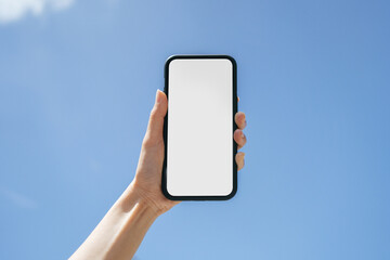 Women hand holding mobile phone with blue sky background in day time. White empty space mobile display. Smartphone blank screen mock up image.