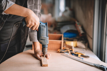 Close up of male mechanic holding electric cordless screwdriver drill with wood screw in the factory. Working with the screw. Professional carpenter.