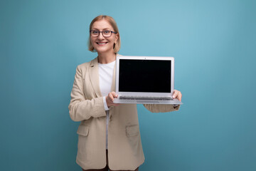 middle-aged mature woman in jacket masters new technique using laptop on studio background with copy space