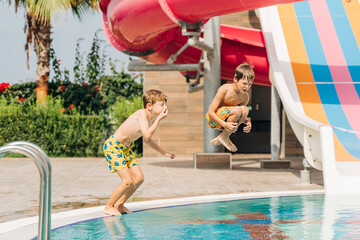 Two brothers Childs jumping and playing in swimming pool at sunny day. Kids friends boys refreshing...