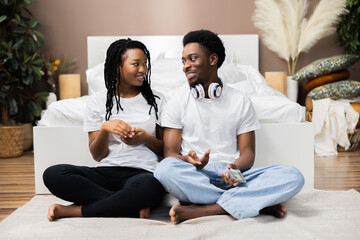 Fototapeta premium Adorable cheerful young African American man and woman couple at home holding money in hands talking discussing purchase. Happy girl earning a lot of money haigh salary.
