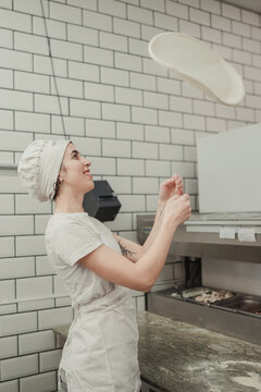 Woman tossing pizza dough in the air while kneading it