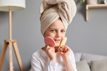 Children beauty. Cute adorable little girl with towel on head sitting in bedroom holding cosmetic...