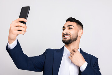 Happy delighted turkish indian middle eastern man guy buisnessman in ellegant suit holding modern new cellphone in hands taking picture selfie speaking with family wife via video link chat time.
