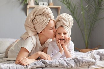 Motherhood, childhood, parenthood. Loving mother and daughter laying in bed wearing towel posing in...
