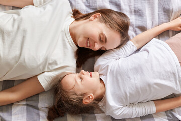 Fototapeta na wymiar Smiling charming mother and daughter resting in bed enjoying weekend talking in the morning wearing white t-shirts happy family relationship motherhood.