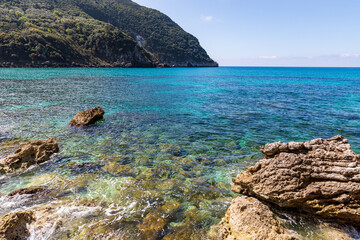 A beautiful landscape of the coast of the island of Corfu in the Ionian Sea of the Mediterranean in Greece. Pure blue clear water washes over the shores of the Greek island.