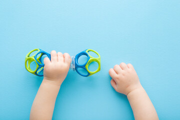 Baby boy hands playing with colorful rattle dumbbell on light blue table background. Pastel color. Closeup. Point of view shot. Toy of development for infant. Top down view. - obrazy, fototapety, plakaty