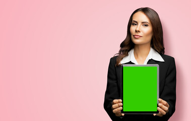 Portrait of young brunette businesswoman showing tablet pc, touchpad, with green chroma key screen, on rose pink background. Confident attractive business woman at office.