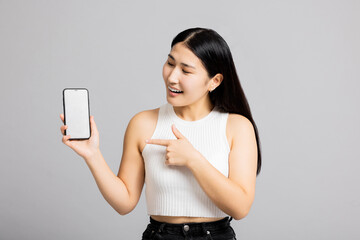 Delighted beautiful yong asian woman in basic clothes holding smartphone white screen showing at camera standing on grey background in studio isolated.