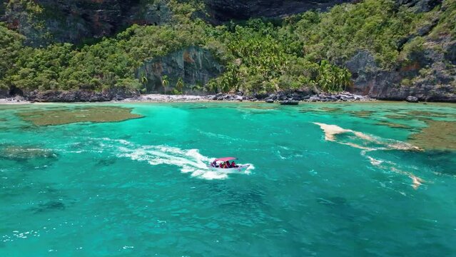 Tourist boat sailing in turquoise sea waters of Playa Fronton beach, Samana in Dominican Republic. Aerial backward