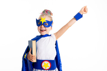 Delighted cute kid wearing superhero mask and costume holding book in hands ready to school standing on white background in studio having fun.