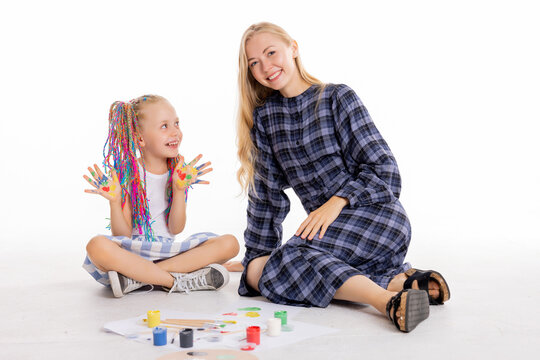 Happy young family cocnept mother with school daugter with colorful braids sitting on white floor painting using painting art tools drawing having fun posing for back to school concept.