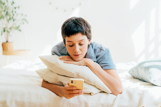 Young attractive woman chatting on the phone while lying lazy on the bed.