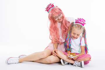 Young modern mom with pink wig and glasses spending time with preschooler funny daughter sitting in...