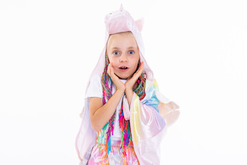 Close-up shot of surprised daughter wearing unicorn hat and colorful braids holding hands near face standing on white ackground in studio isolated posing while shooting process.