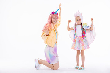 mother and daughter in colorful clothes wearing pink wig and unicorn headband and hat looking at camera dancing posing in funny poses while shooting process for stylish shop magazine.