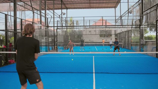 A lot of people playing tennis outdoor court. Young adult player serve ball opponent. Racket sport game. Athlete team group hit workout outside arena. Sportsmen health care. Woman person fit exercise.