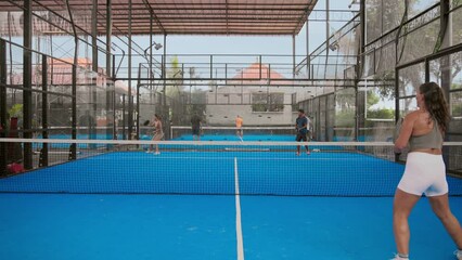 A lot of people play tennis outdoor court. Young adult player serve ball opponent. Racket sport game match. Team hit workout outside arena. Sportsman health care. Woman person fit exercise. Girl train