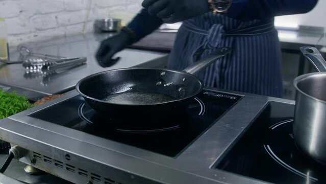 Chef cook sets stewpan on electric stove, puts rosemary, garlic and meat steak on frying pan. Making delicious dishes process. Restaurant with gourmet cuisine. Public catering concept. Tracking shot.